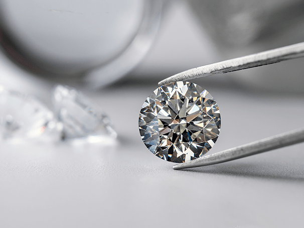 Round brilliant diamond held by tweezers, illustrating expert appraisal services at Qollateral.