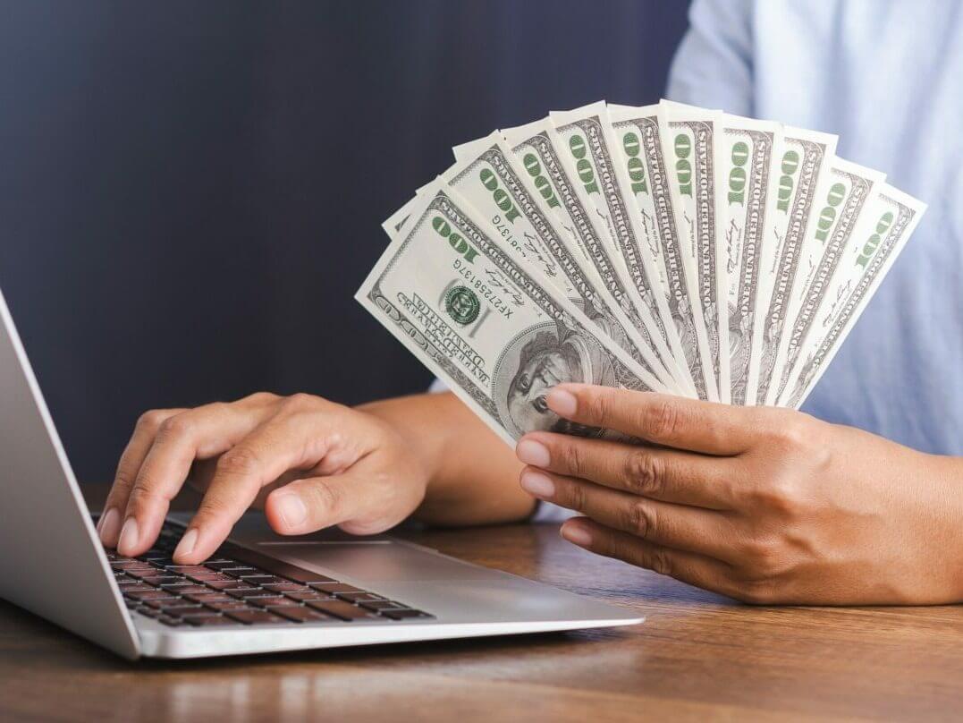 Person holding cash in front of a laptop symbolizing fast, secure online collateral loans offered by Qollateral.