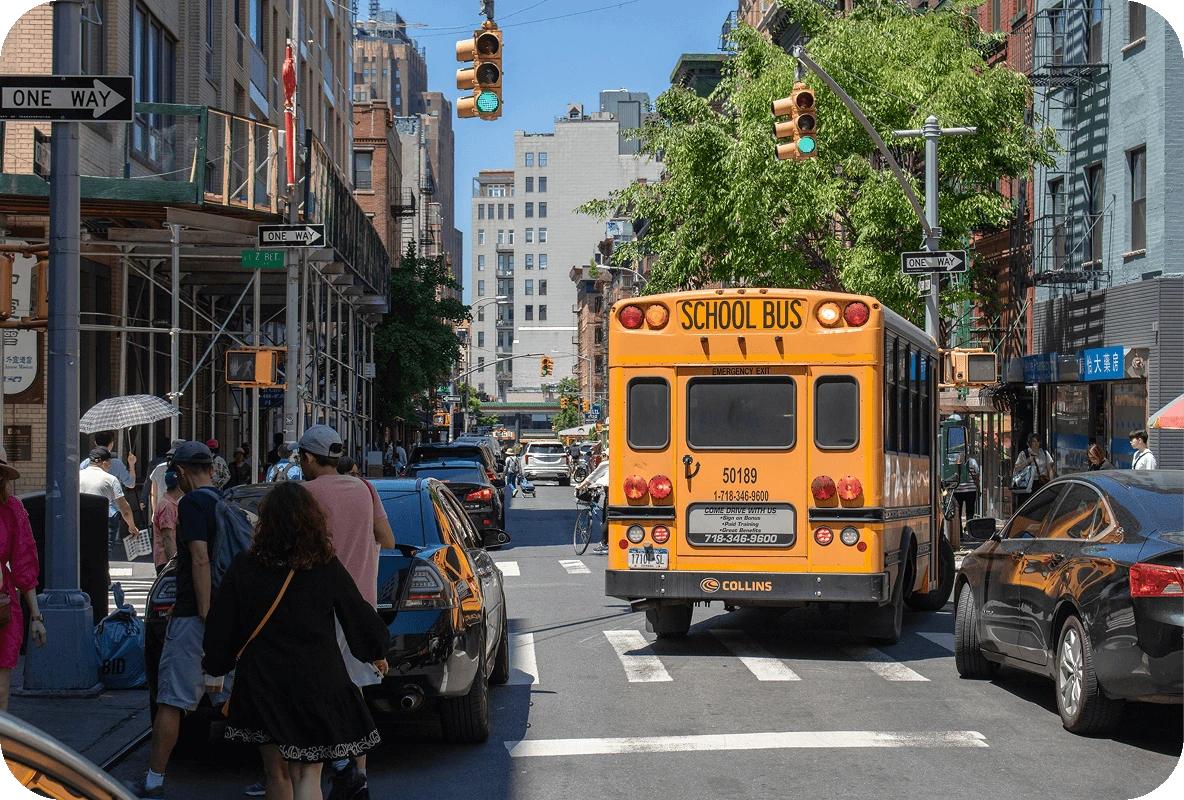 Yellow school bus driving down a busy city street with pedestrians and cars