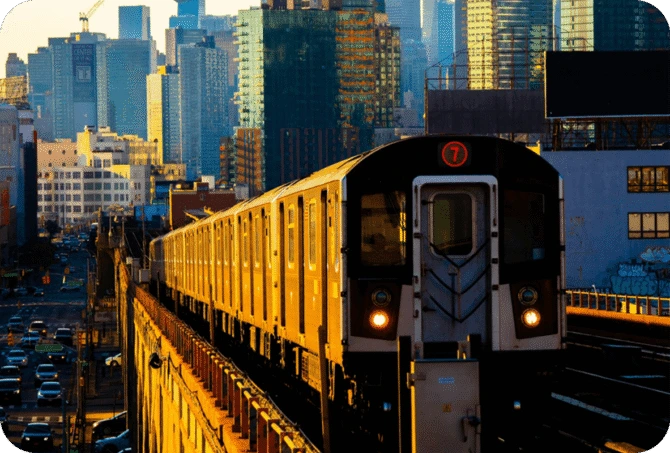 NYC Subway 7 train approaching with Manhattan skyline in the background at sunset