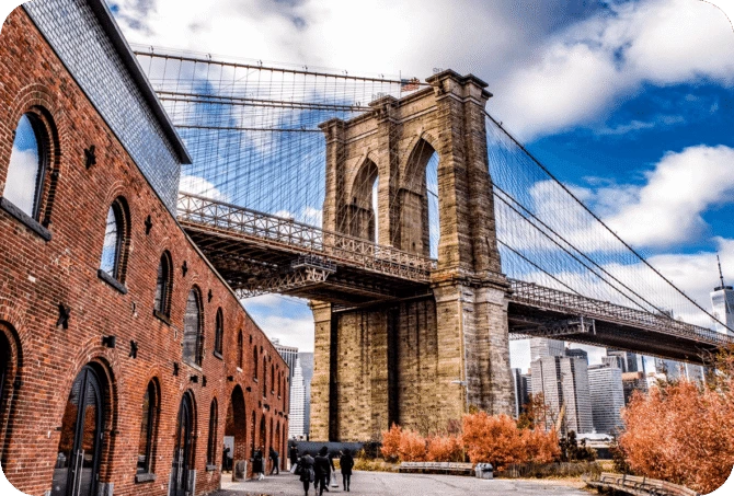 View of the Brooklyn Bridge from DUMBO with a historic red-brick warehouse in the foreground and Manhattan skyline in the background