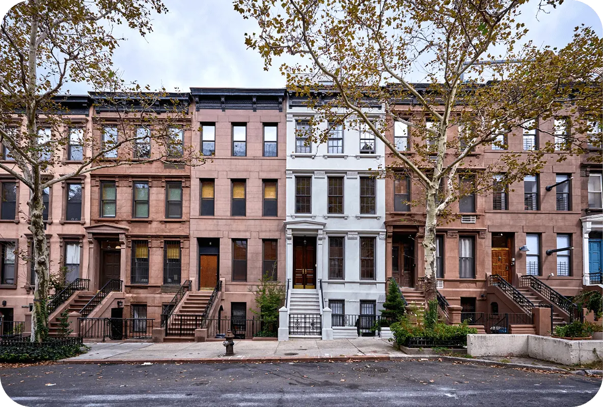 A row of historic brownstone townhouses with trees lining the street in front