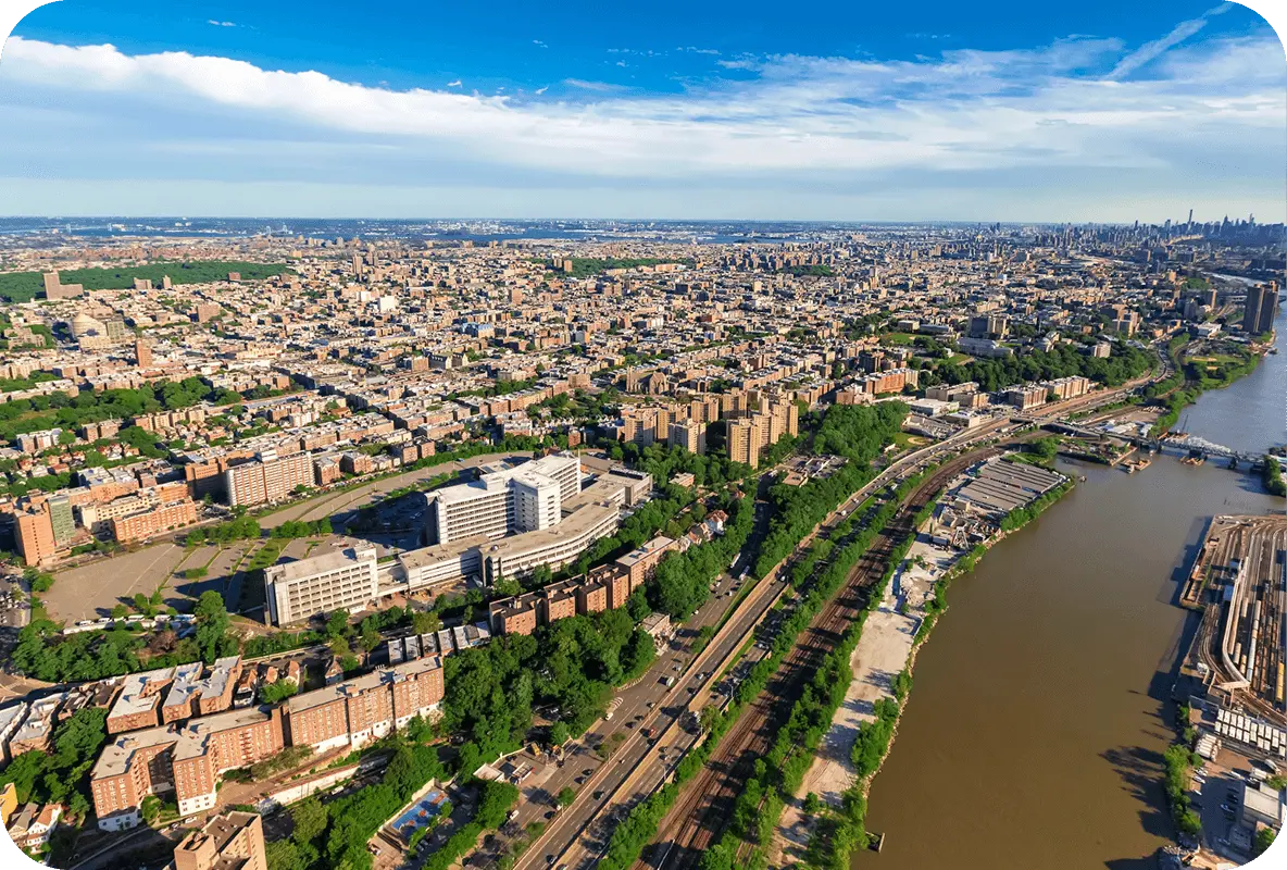Aerial view of the Bronx with buildings, highways, and the Harlem River under a blue sky