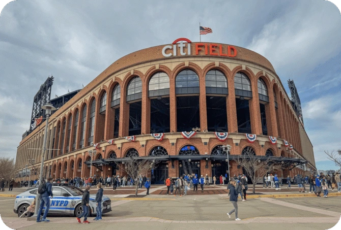 Exterior view of Citi Field in Queens, New York, with crowds of people and an NYPD vehicle in the foreground