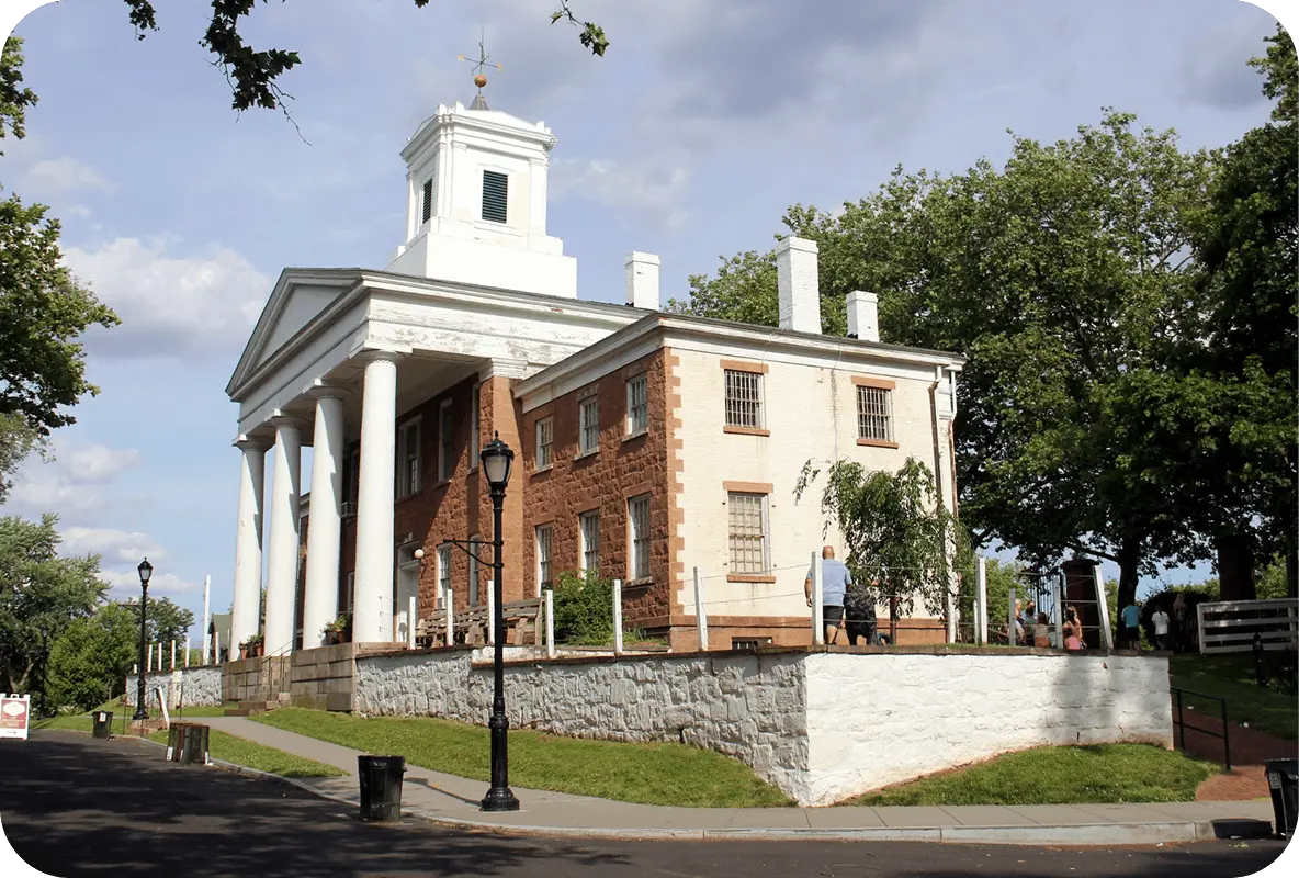 Historic red-brick building with white columns and a cupola surrounded by trees