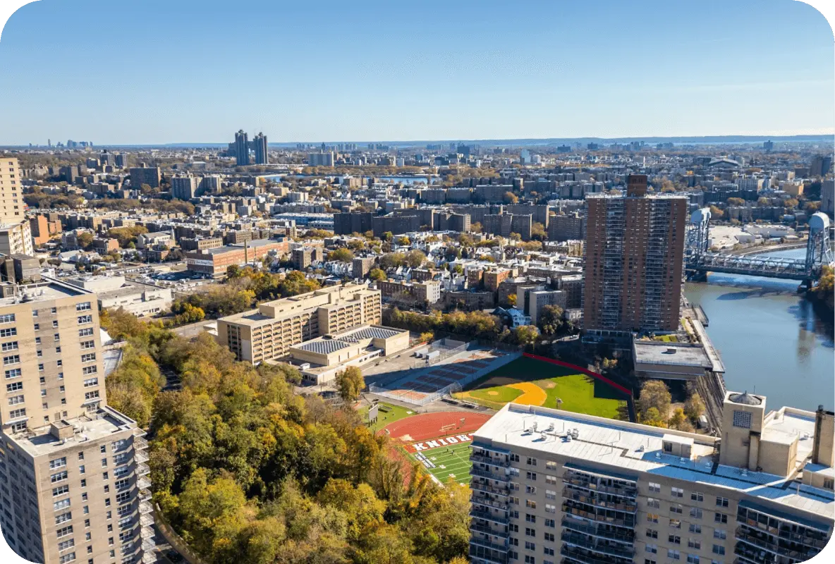 Aerial view of the Bronx, New York, featuring high-rise buildings, a school athletic field, and the Harlem River