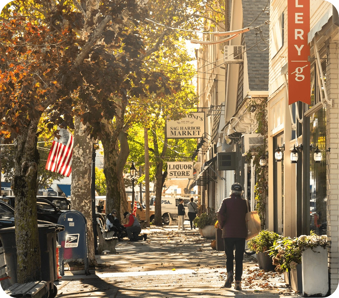 Tree-lined sidewalk with storefronts and pedestrians in a small town setting