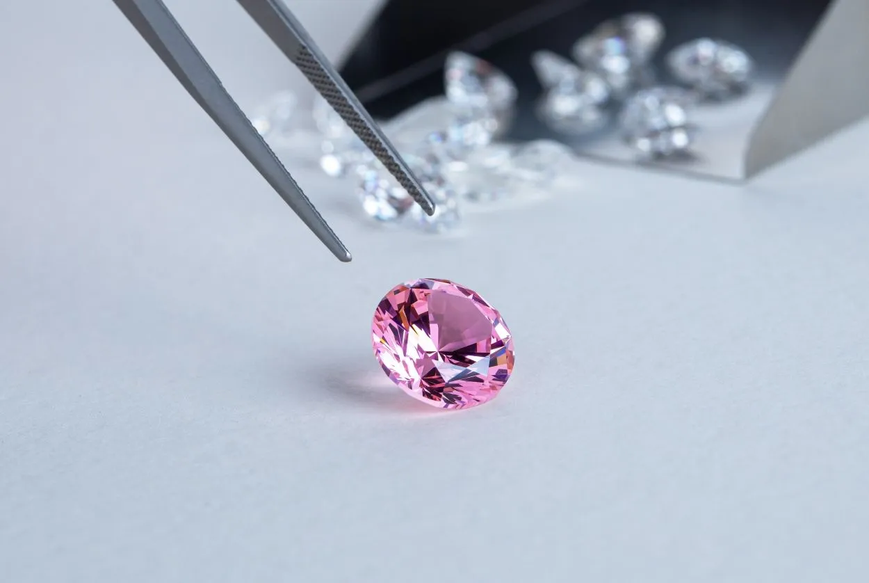 Close-up of a pink gemstone being examined with tweezers during a professional jewelry appraisal at Qollateral.