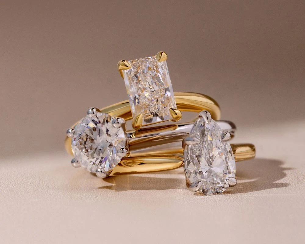 Close-up of three diamond engagement rings in yellow and white gold on a neutral background.