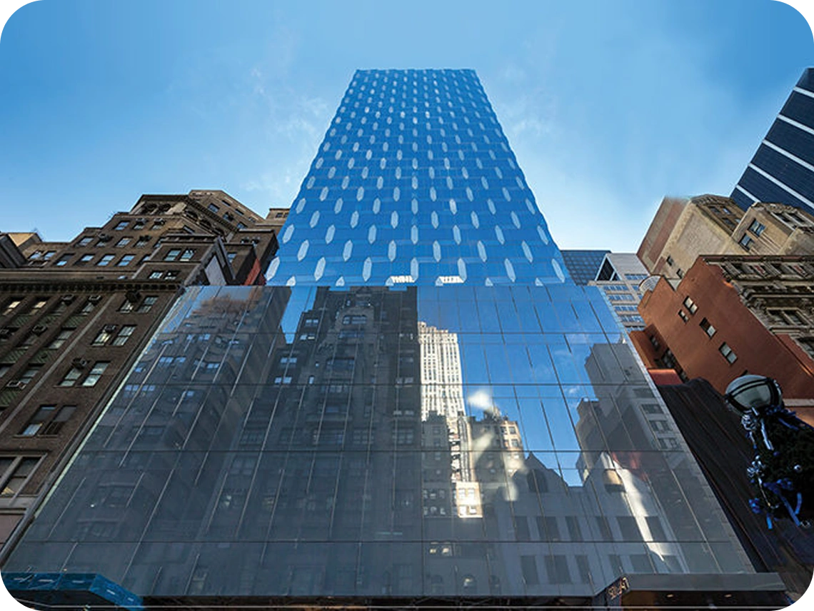 Modern glass skyscraper viewed from below with reflective facade and surrounding buildings